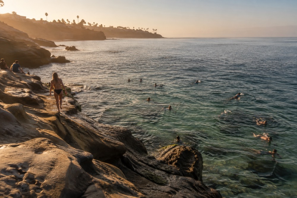 Swimmers and snorkelers in clear green water near La Jolla Cove's rocky shore