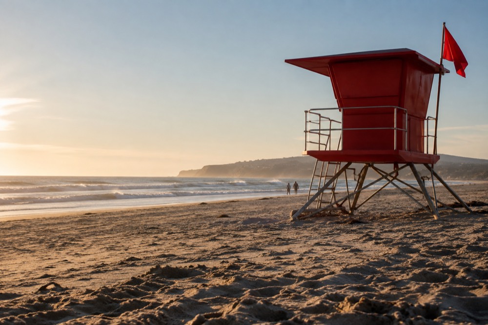 Red lifeguard tower standing on a wide beach with a red warning flag