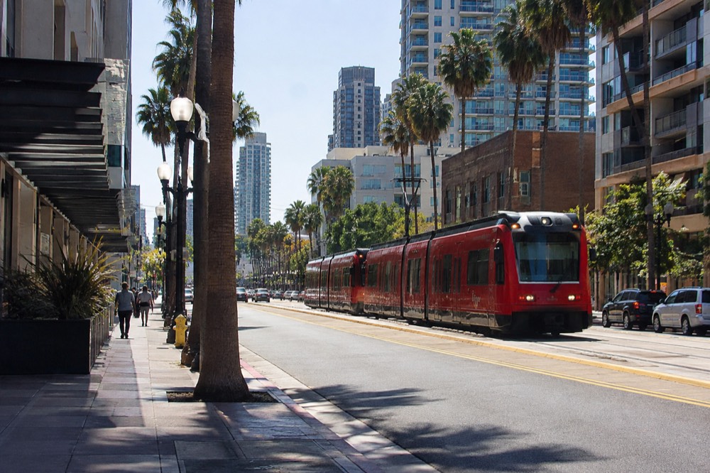 Red trolley passing through downtown San Diego street with palm trees