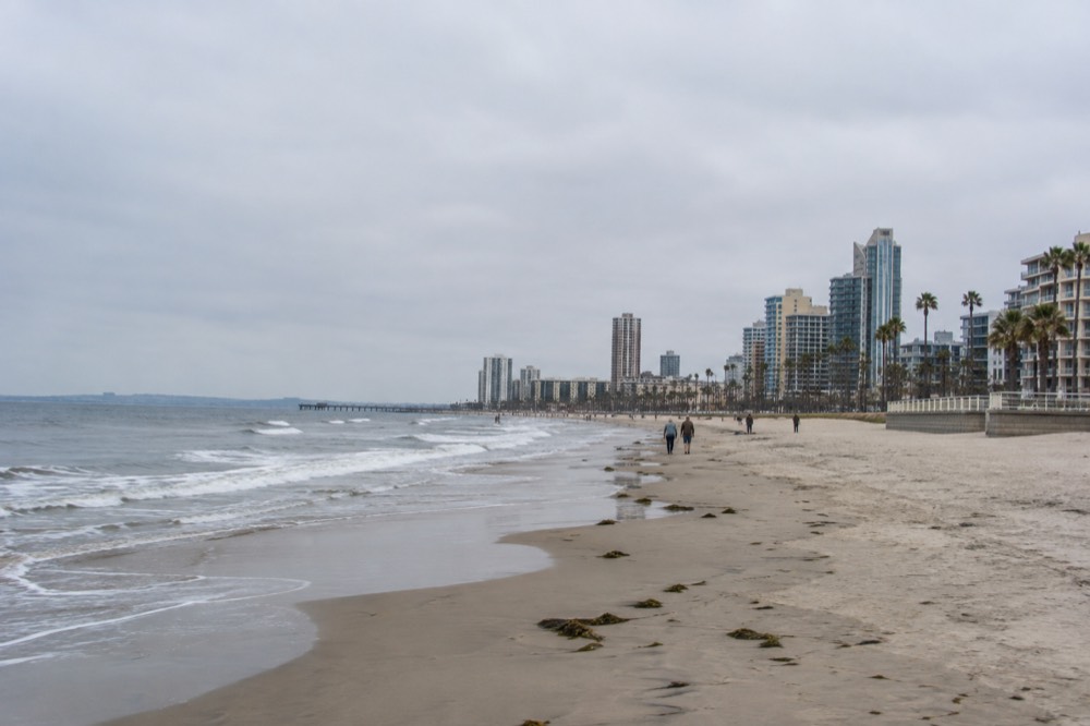 A wide sandy beach with a boardwalk and few people on a mild morning