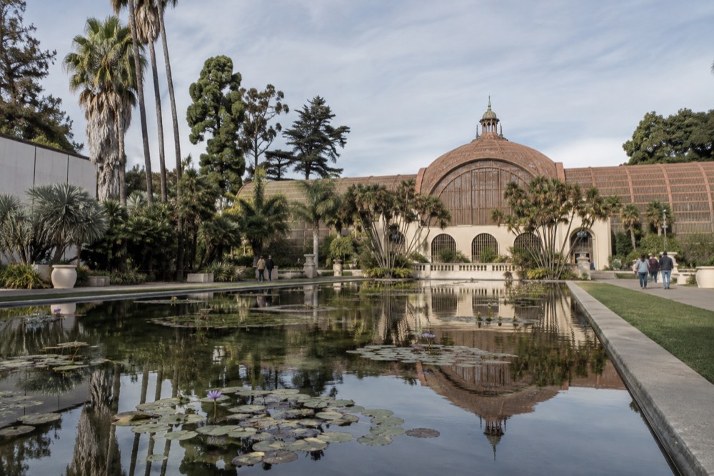 A lily pond reflecting a domed glass conservatory surrounded by greenery