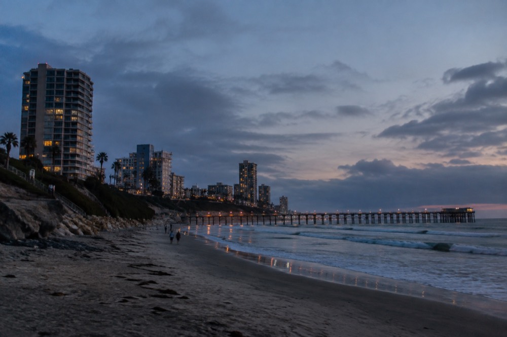 Long sandy beach with a wooden pier and small waves rolling in