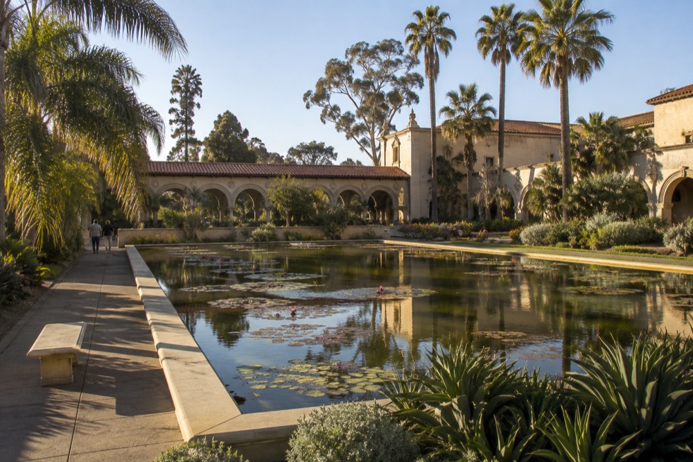 Balboa Park gardens with a lily pond, historic arched building and palm trees under a blue sky