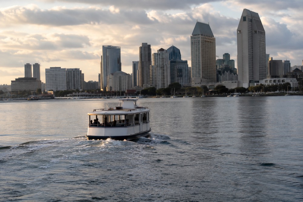 Small tour boat on calm bay water with the city skyline behind it in late afternoon light